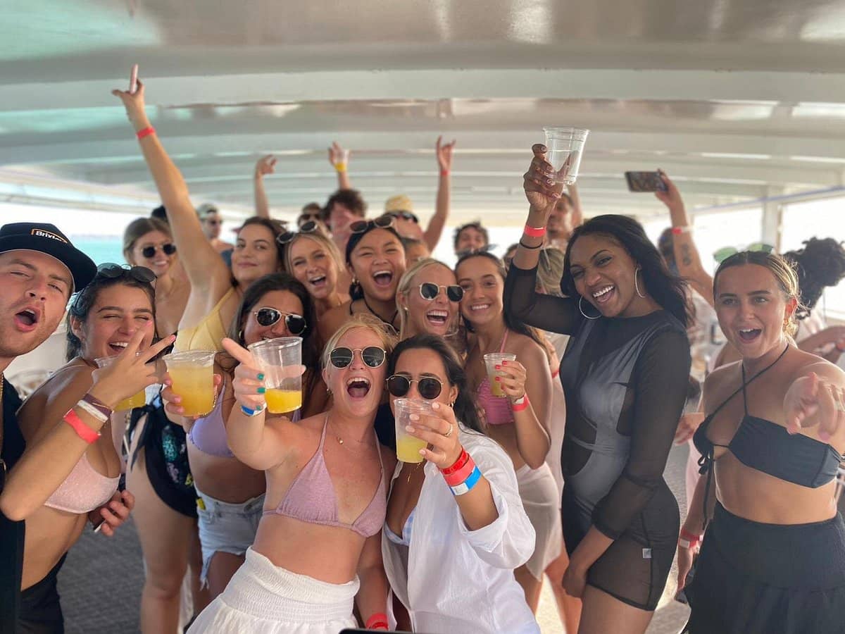 Group of friends laughing, cheering and celebrating on a private yacht charter in Dubai. lot of guest are holding glasses in a yacht and smiling with book yacht rental dubai